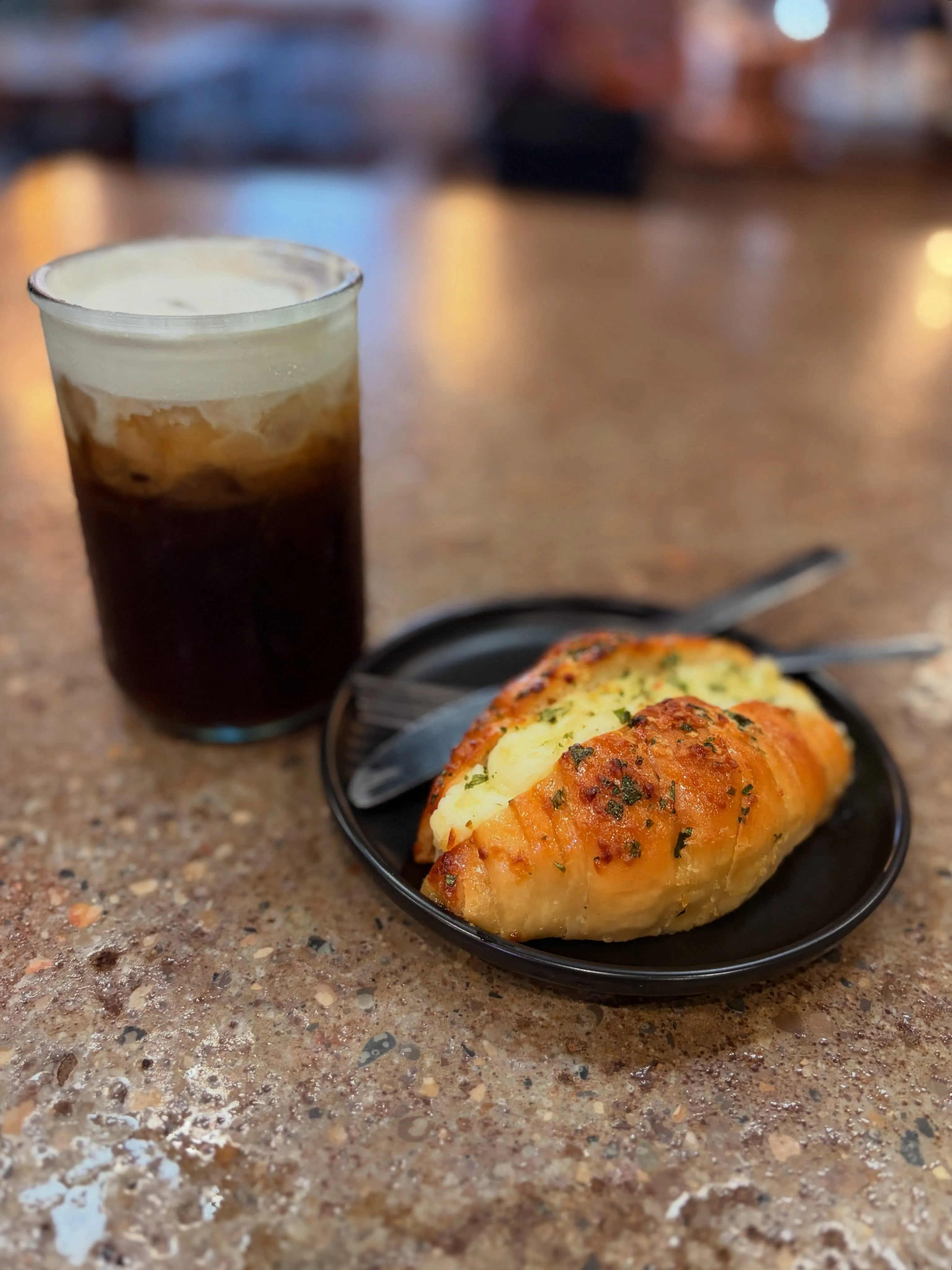 A cold brew under a cream float beside a cheese and herb croissant
