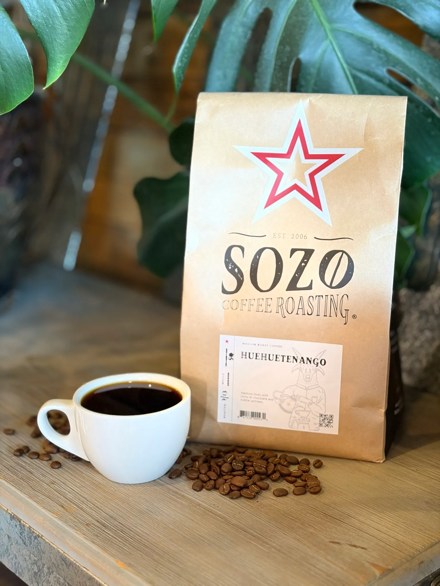 A bag of Sozo Coffee Roasting Huehuetenango beside a cup of black coffee and loose beans