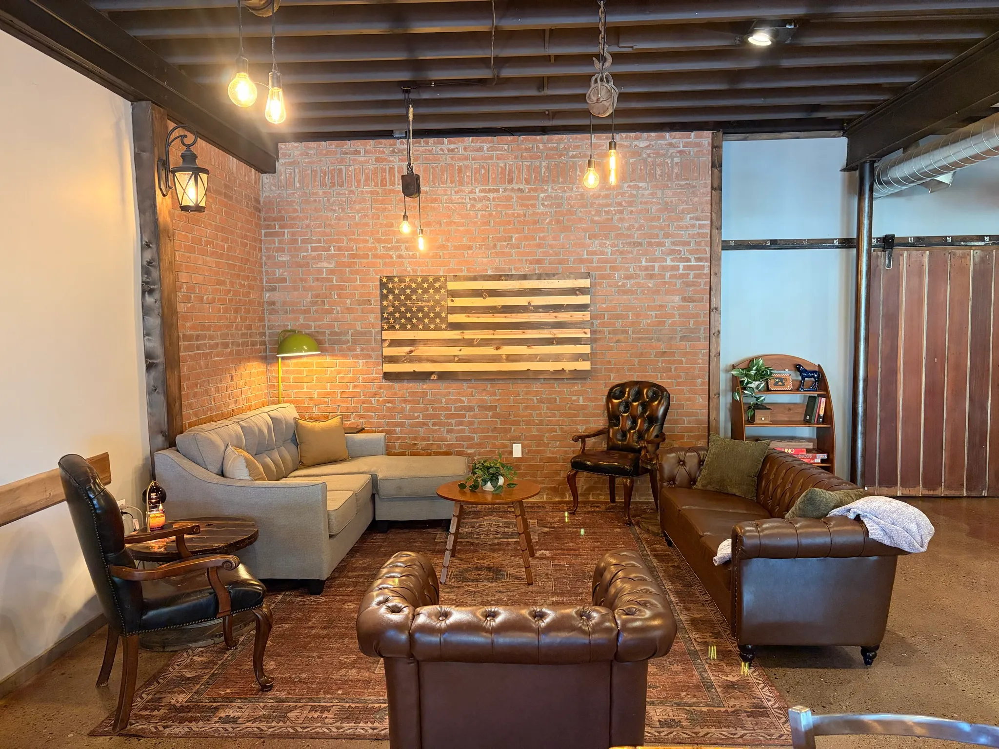 Leather chesterfield sofas and armchairs around a rug in The Room, under exposed beams and an exposed brick wall